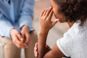 Close up view of african american girl with hand near eye crying during consultation with blurred psychologist