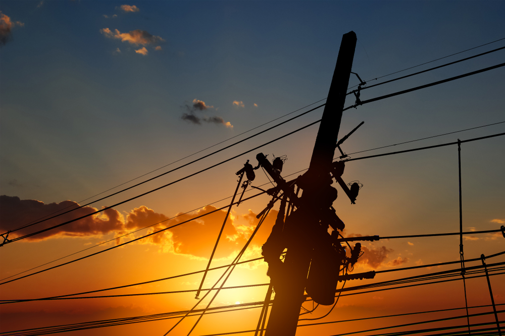 silhouette of an electrician working on a power pole with a sunset sky in background