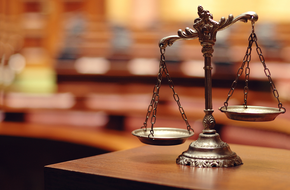 selective focus of scales of justice on a table with a blurred courtroom background