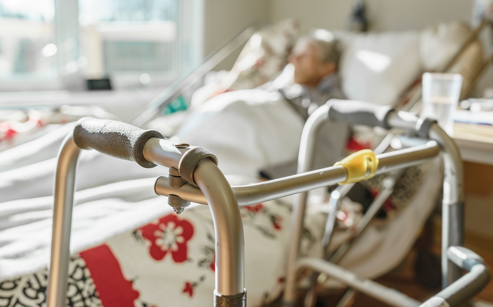 blurred sick elderly woman in a hospice bed with selective focus on a walker in the foreground